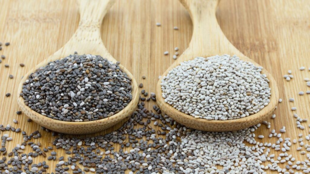 Black and white chia seeds in wooden spoons on a bamboo surface.