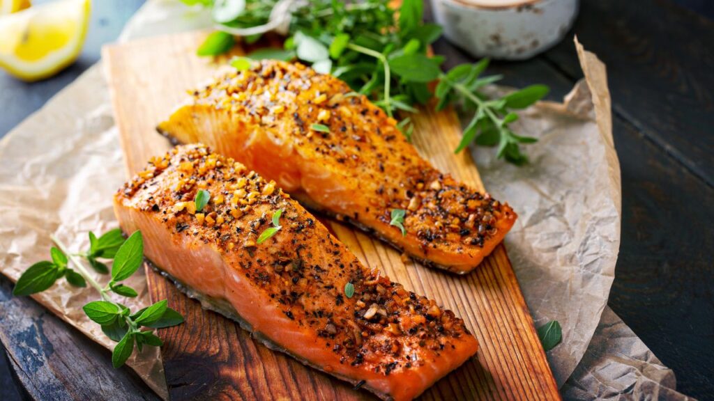 Two baked Za’atar salmon fillets on a rustic wooden board, garnished with fresh oregano and served with lemon wedges. This Mediterranean-inspired dish is rich in omega-3s, antioxidants, and fertility-boosting nutrients.