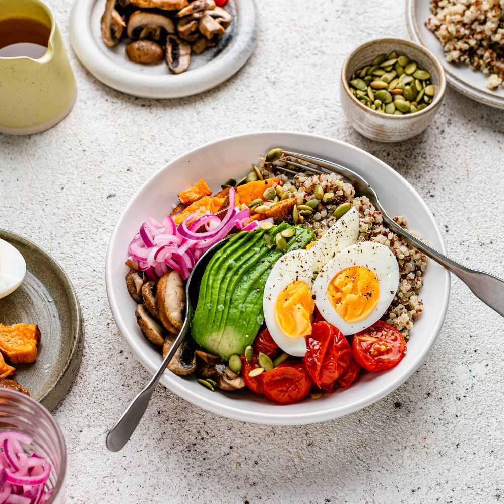 Fertility-friendly abundance bowl with quinoa, roasted sweet potatoes, sautéed mushrooms, cherry tomatoes, avocado, pickled onions, soft-boiled eggs, and pumpkin seeds. A nutrient-rich meal designed to support fertility health.