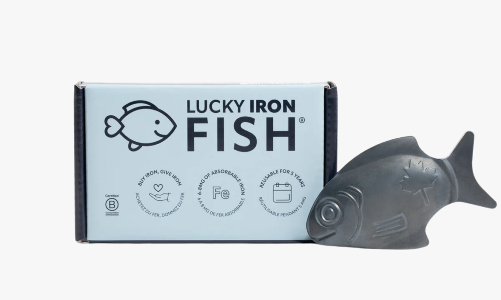 The Lucky Iron Fish, a reusable iron cooking tool, displayed next to its packaging. The box highlights key benefits, including providing 6-8mg of absorbable iron per use, being reusable for up to 5 years, and supporting the Buy One, Give One initiative. The fish-shaped iron piece features a maple leaf design, symbolising its Canadian origin. A simple and sustainable way to boost iron levels, perfect for vegans and those looking to fortify meals naturally.