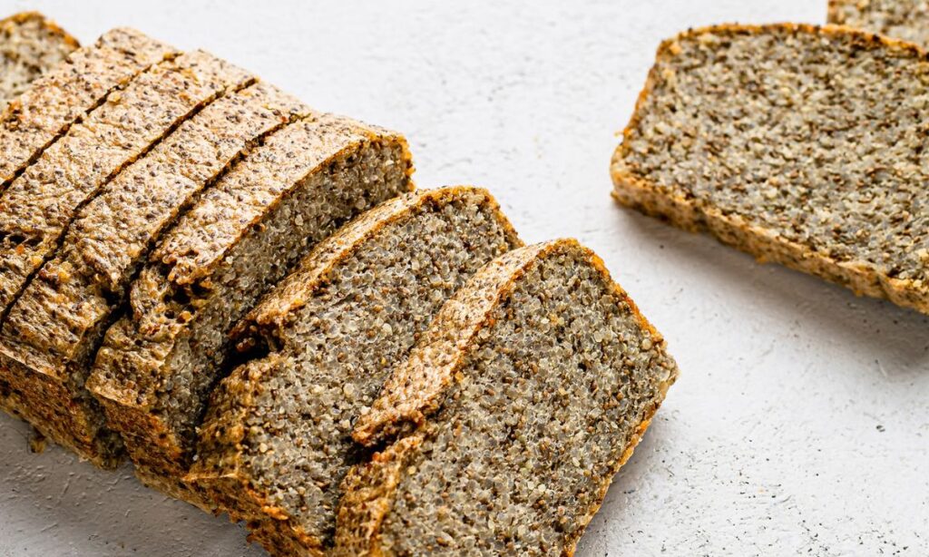 Close-up of a sliced seed and nut gluten-free loaf on a light surface, showcasing its dense texture with visible seeds and grains.