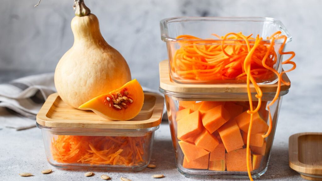 Fresh butternut squash and spiralized carrots stored in glass containers with bamboo lids, a hormone-friendly alternative to plastic for reducing endocrine disruptors.