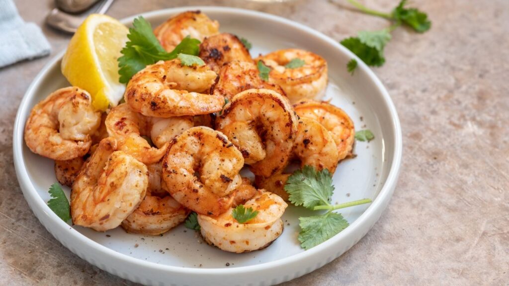 Garlic chilli prawns served in a white dish with coriander leaves and lemon wedge: A zinc-rich food to support sperm production and boost male fertility.