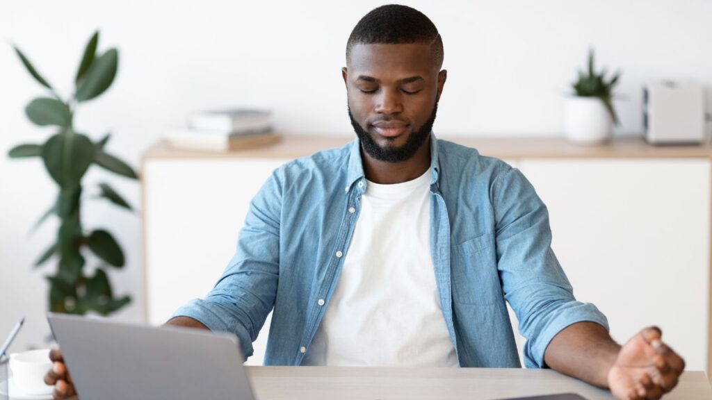 Man meditating at his desk with eyes closed, practising mindfulness: Meditation helps relieve stress, balance hormones, and support male reproductive health