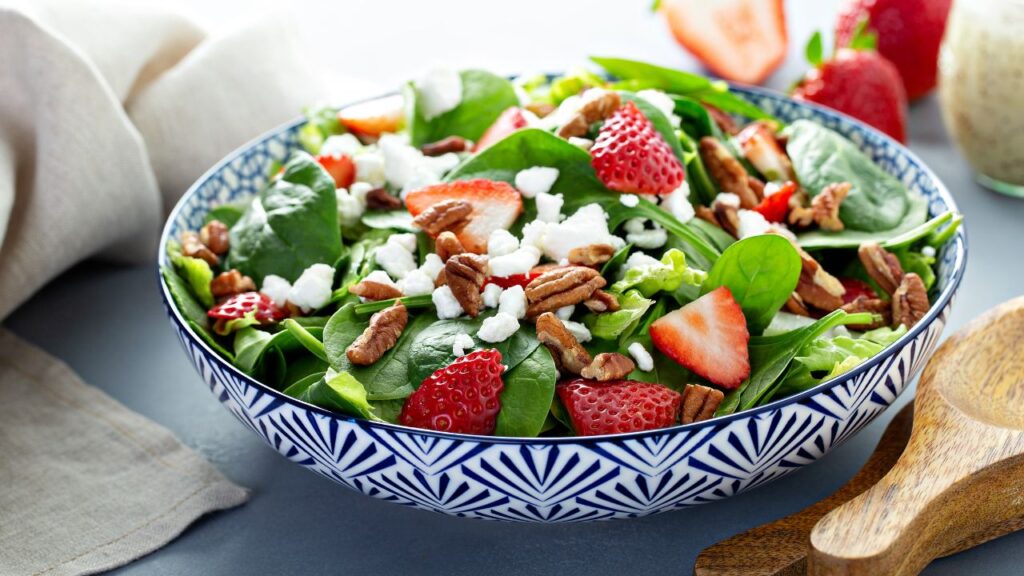 A vibrant strawberry, pecan, and spinach salad served in a blue patterned bowl: A nutrient-packed dish high in vitamin C and vitamin E to support sperm health and motility.