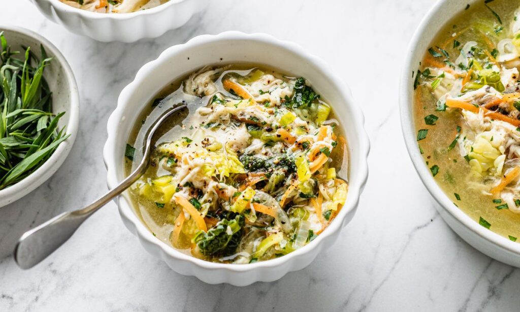 Nourishing chicken and vegetable bone broth in a white bowl, packed with leafy greens, shredded chicken, and herbs – a fertility-boosting meal rich in collagen and essential nutrients.