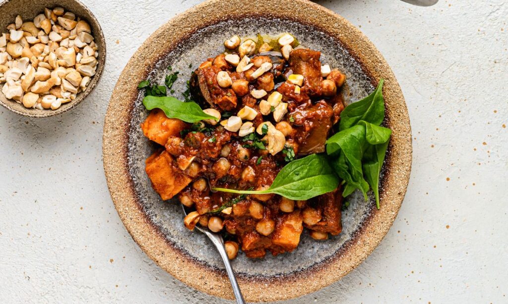 Chickpea and aubergine seven-spice traybake served with fresh spinach and topped with crushed cashews – a nutrient-dense, fertility-boosting meal rich in plant-based protein and fibre.