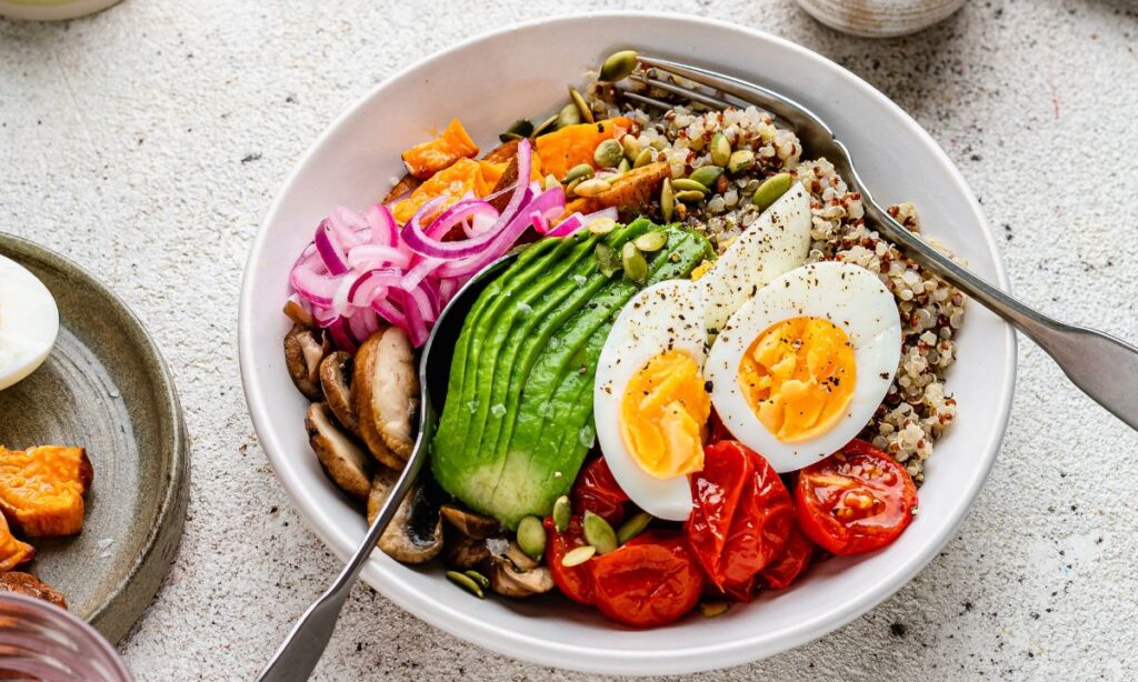 Fertility abundance bowl with avocado, quinoa, boiled eggs, roasted tomatoes, mushrooms, pickled onions, and sweet potatoes – a nutrient-packed meal supporting hormone balance and reproductive health.