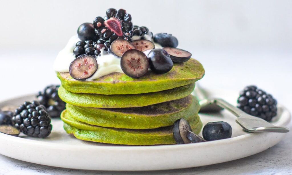 Stack of vibrant green goddess pancakes topped with yoghurt, blackberries, and blueberries – a nutrient-dense, fertility-boosting meal rich in leafy greens and antioxidants.