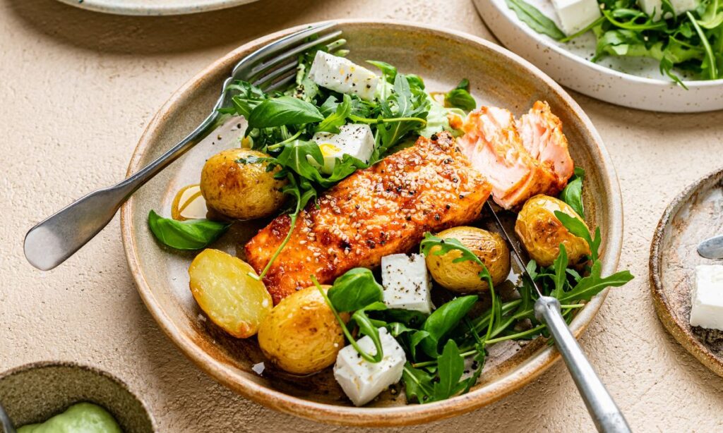 Spiced salmon traybake served with roasted baby potatoes, fresh rocket, and feta cheese – a nutrient-rich, fertility-boosting meal packed with omega-3s.