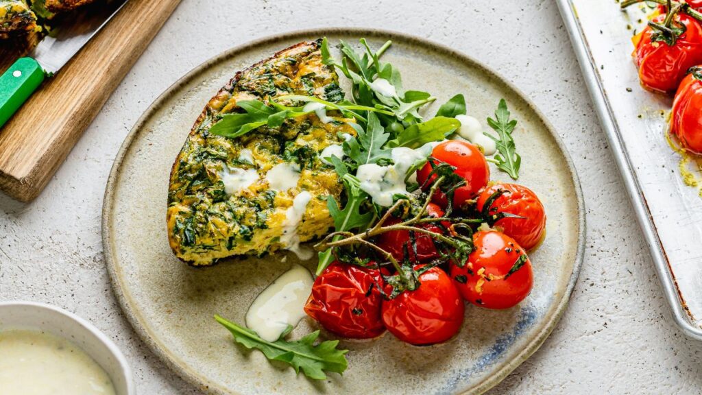 High-protein fertility breakfast featuring a spinach and goat's cheese frittata served with roasted cherry tomatoes and fresh rocket. A nutrient-dense meal rich in protein, healthy fats, and antioxidants to support hormone balance and reproductive health.