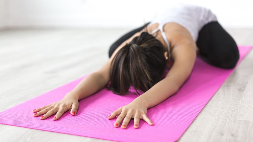 A woman practicing yoga in Child’s Pose on a pink mat, stretching her arms forward in a calming position. This restorative yoga pose helps reduce stress and balance cortisol levels.